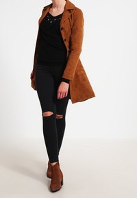 Brun mockakappa med svart topp med glitter, svarta rivna jeans och bruna ankelstövlar. V-ringad design, strukturerad passform, skräddarsytt utseende.