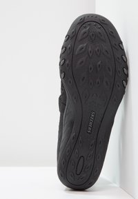 Suela negra de zapatilla con goma texturizada, que presenta un corte ovalado, patrones de hojas distintivos y la marca "SKECHERS".