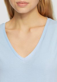 T-shirt azzurro chiaro a scollo a V realizzato in tessuto morbido, caratterizzato da un design pulito e una trama sottile, che mette in risalto il collo e le spalle.