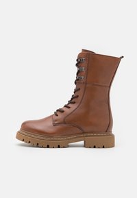 Hnědé kožené kotníkové boty na šněrování s masivní podrážkou, vybavené kovovými očky a mírně zaoblenou špičkou. Texturovaný povrch a detaily prošívání.