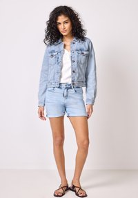 Giacca di jeans azzurro chiaro con chiusura a bottoni e tasche sul petto, abbinata a pantaloni shorts in denim azzurro chiaro. Design semplice, vestibilità casual.