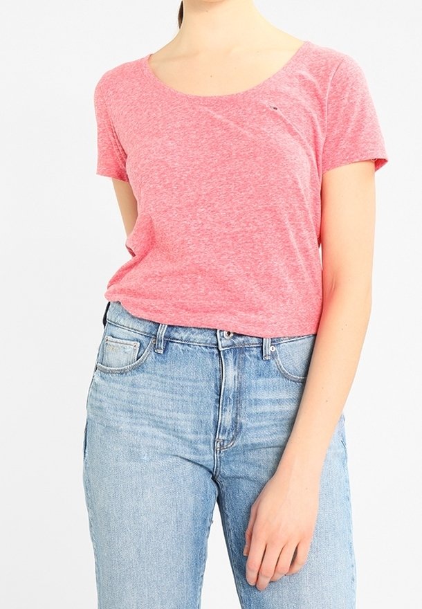 Camiseta de manga corta en color rosa con textura jaspeada, con escote redondo y un pequeño logo en el pecho, combinada con vaqueros de un azul claro.