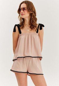 Svetloružový top bez rukávov s čiernymi ramienkami, s viacvrstvovým dizajnom a čiernym zúbkovaným okrajom; spárovaný s vyhovujúcimi šortkami.