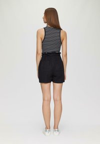 Shorts en lin noirs avec une taille ondulée et deux poches arrières, associés à un haut sans manches à rayures noir et blanc. Chaussures argentées.
