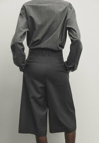 Chemise grise texturée avec des rayures verticales, rentrée dans des culottes taille haute assorties. Les deux pièces ont des formes ajustées et des lignes épurées.