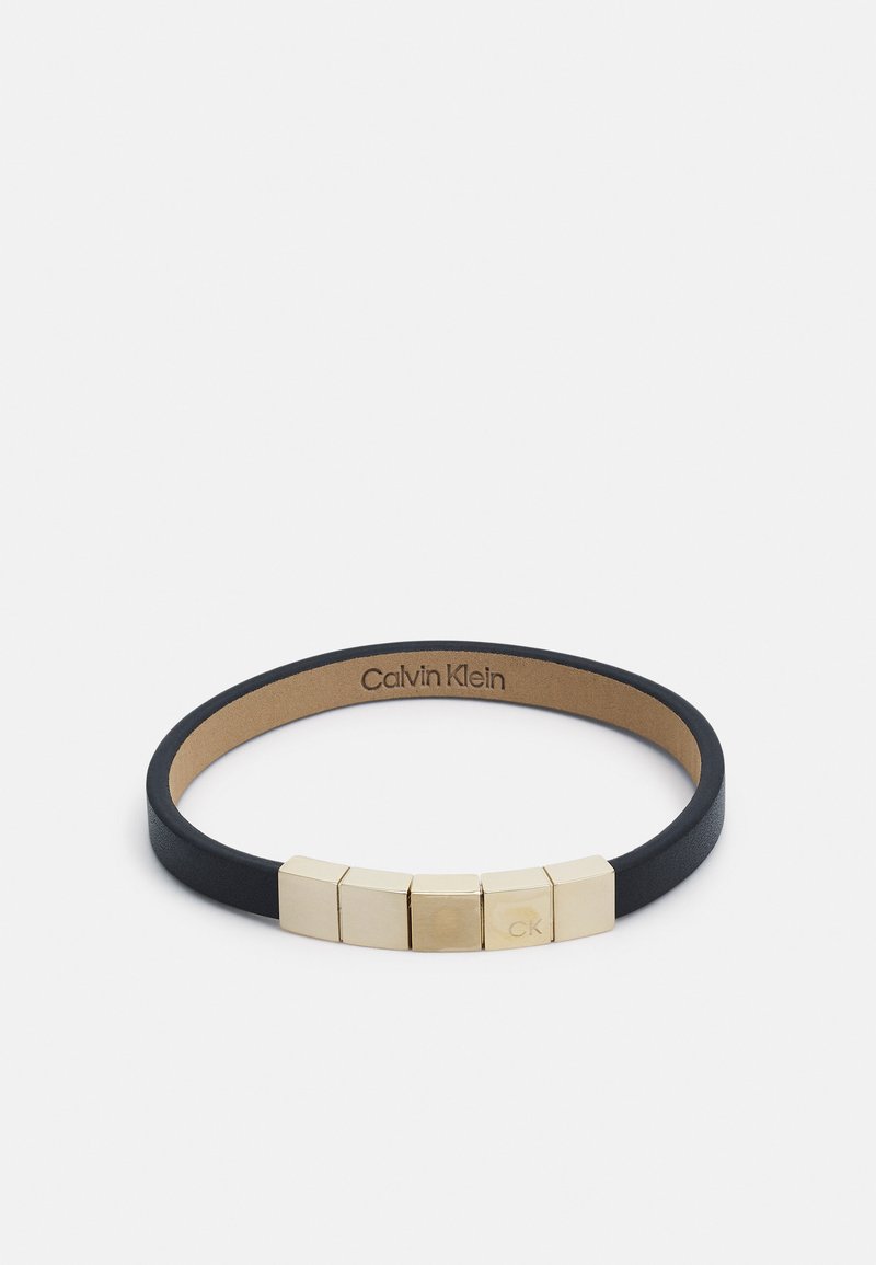 Pulsera de cuero negro con cinco acentos geométricos dorados y grabado "CK". Textura suave con un diseño minimalista.