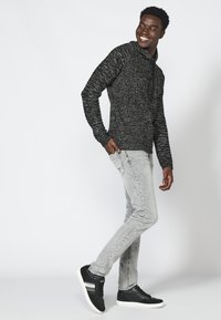 Felpa a cappuccio a maglia nera e bianca con zip, abbinata a jeans grigi chiari e sneaker nere con accenti bianchi.