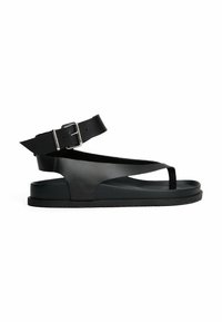 Sandal in pelle nera con design minimalista, dotata di una larga cinghia alla caviglia e un inserto tra le dita. Suola piatta con grip testurizzato e fibbia regolabile.