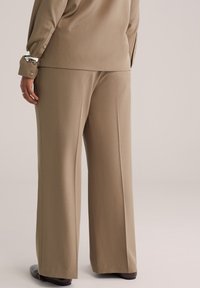 Bež široke hlače z ravnim krojem iz gladkega materiala, z diskretnimi naborki in čistim robom, kombinirane z ujemajočo se zgornjo majico.