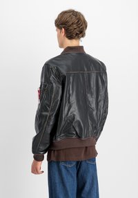 Černá kožená bomber bunda s žebrovaným límcem a manžetami. Obsahuje viditelné švy, boční kapsu s kovovými detaily a volný střih.
