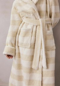 Randig plyschbadrock i kräm och beige. Mjuk textur med sjalkrage, bälte och två framfickor. Långa ärmar och knälång design.