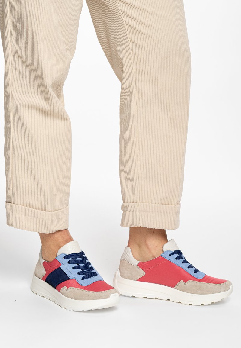 Füße in beigen, hochgekrempelten Cordhosen und mehrfarbigen Turnschuhen in Rot, Blau, Marineblau und Weiß mit dicken weißen Sohlen.