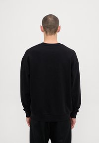 Felpa nera oversize con maniche lunghe, collo rotondo e polsini a coste. Texture liscia con una vestibilità comoda. Senza loghi o motivi visibili.