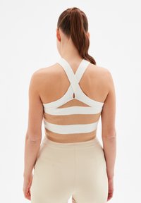 Sujetador deportivo de rayas beige y blancas con un diseño de espalda cruzada. La tela es suave y elástica. Pantalones beige ajustados a juego.
