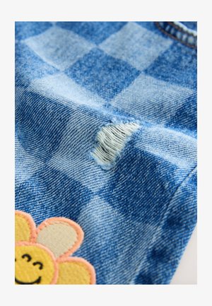 Jeans tkanina ima karo vzorec, z obrabljenim luknjo in rumeno vezenino cvetja blizu dna, ki dodaja barvni kontrast.