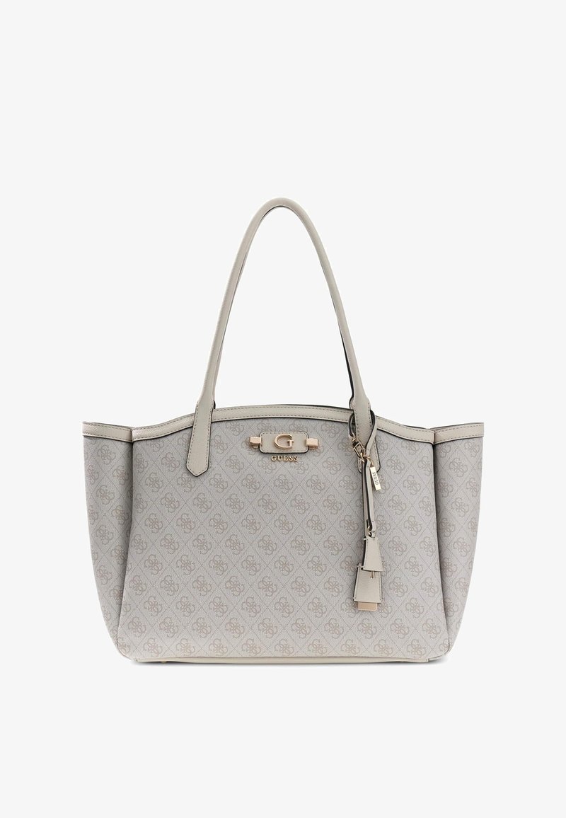 Sac fourre-tout beige Guess avec doubles poignées, motif monogramme, plaque logo dorée et étiquette décorative suspendue sur fond blanc uni.