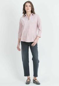 Vaaleanpunainen kauluspaita, jossa on pystysuorat raidat, pitkät hihat ja laskos edessä, yhdistetty tummiin farkkuille ja mustiin niittikenkäisiin.