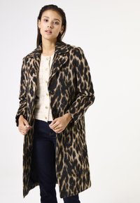 Leopardenprint wolwantenk met een geknipt kraag, enkelvoudige knoopsluiting en lange mouwen, gecombineerd met een lichte, gestructureerde top.