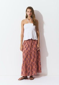 Top blanco sin tirantes con fruncidos, combinado con una falda larga maxi estampada en tonos de rosa y púrpura. Sandalias marrones con tiras completan el conjunto.