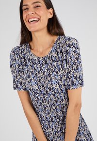 Vestido de manga corta con un patrón floral en azul oscuro, azul claro y beige. La tela tiene una apariencia texturizada y plisada.