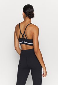Black sports bra with crisscross straps and a contrasting white band, paired with high-waisted black leggings, smooth fabric, fitted design.