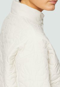 Wit gewatteerd jasje met een hoge kraag, textuurpatroon met subtiele krommingen en een trekkoorddetail bij de hals.