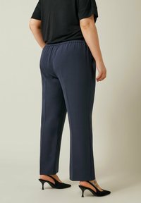 Navyblauwe elastische broek met een rechte pijp, gecombineerd met zwarte hakken. Zachte stof met een gladde textuur.