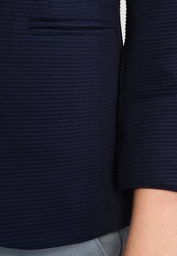 Sako z texturované látky v námořnické modři, slim fit, s viditelnou boční kapsou a hladkým límcem. Materiál vypadá jako pruhovaný.