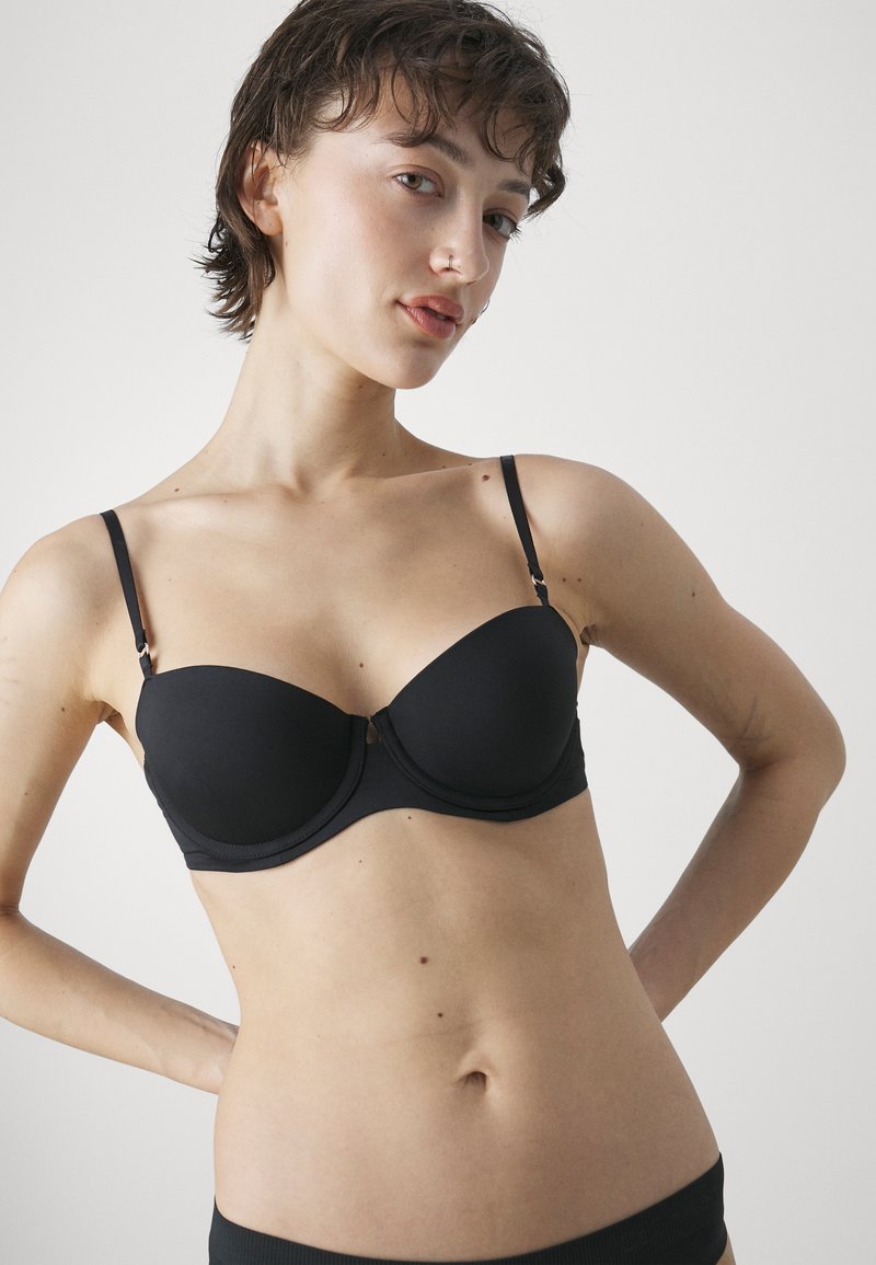 Schwarzer gepolsterter Unterwire-BH mit verstellbaren Trägern und glatter Textur. Verfügt über ein nahtloses Design und einen kleinen metallischen Akzent in der Mitte.