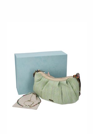 Un bolso de hombro verde claro con estampado y ribete beige está junto a una caja azul, un collar de cuentas y una cadena dorada sobre una tela de exposición.