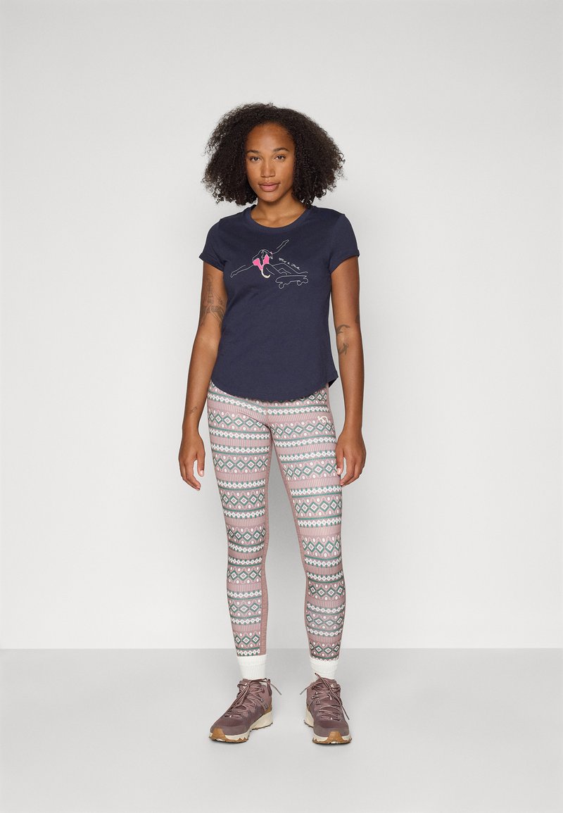 Marineblauses Baumwoll-T-Shirt mit grafischem Druck, kombinierbar mit gemusterten Leggings mit geometrischen Designs in Pastellfarben und braunen Wanderschuhen.