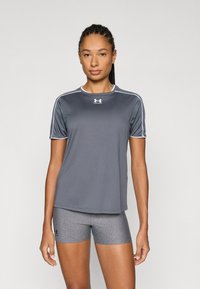 Szürke sportos rövid ujjú póló fehér kiemelésekkel, szürke rövidnadrággal párosítva. Az anyag simának és rugalmasnak tűnik. Látható az Under Armour logó.