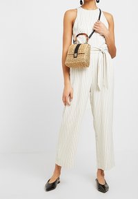Jumpsuit leggero a righe verticali in bianco e beige con vita legata. Abbinato a una piccola borsa intrecciata e ballerine nere a punta.