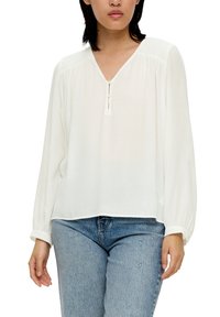 Blouse blanche à manches longues avec un col en V et une fermeture à boutons à l'avant. Fabriquée en tissu léger avec une texture lisse.