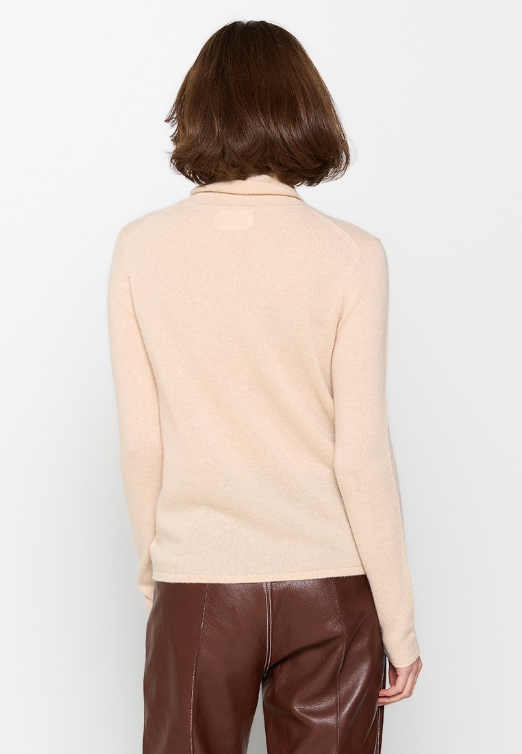 Beige Strickpullover mit langen Ärmeln und hohem Kragen, der eine weiche Textur, eine schmalen Schnitt und minimale Details auf der Rückseite aufweist.