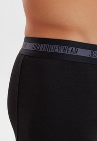 Schwarze Unterwäsche mit einer glatten Textur und einem kontrastierenden dunkelgrauen Bund, der mit dem dezenten Aufdruck "JBS UNDERWEAR" versehen ist.