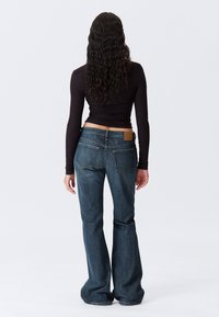 Donkerblauwe flared jeans met twee achterzakken en een leren label dichtbij de tailleband. De stof heeft een subtiele textuur en een klassiek ontwerp.