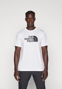 Hvit bomulls t-skjorte med "THE NORTH FACE" i fet sort skrift og en buet logo, rund hals og korte ermer.