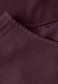 Tissu bordeaux au toucher lisse, avec un bord replié et un léger éclat. Le design comprend une couture plate le long de l'encolure.
