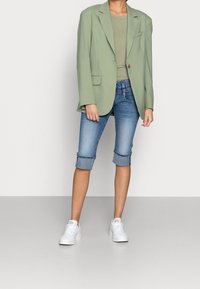 Světlezelený blazer přes šedý top, doplněný o ohrnuté džíny šortky. Bílé tenisky dokončují outfit. Hladká textura, uvolněný střih.