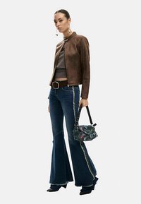 Brown leather jacket, gray top, blue flared jeans with stitching details, and a black handbag with colorful accents. Black high-heeled boots.