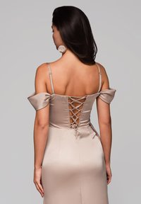 Satiiniselle iltamekko pehmeässä beigeessä, jossa on olkaimeton malli, nauhakiinnitys selässä ja sulava, vartalonmyötäinen siluetti.