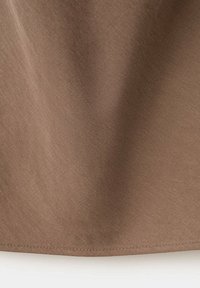 Tissu marron avec armure diagonale visible et couture le long du bord inférieur, montrant la texture et le tombé.
