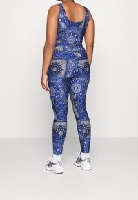 Blue patterned bodysuit featuring a bandana design. Smooth texture with a fitted shape, paired with white athletic shoes.