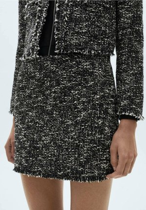 Zwart-witte getextureerde tweed rok en bijpassend cropped jasje met rafelige randen, gedragen door een staand persoon.