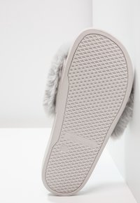 Semelle d'une pantoufle gris clair avec un dessous en caoutchouc texturé et un bord en fausse fourrure duveteuse sur le côté.