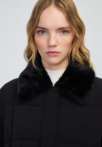 Zwarte gewatteerde jas met een weelderige zwarte bontkraag, met een gestructureerd ontwerp en een soepele textuur. Eenvoudige, minimalistische esthetiek.