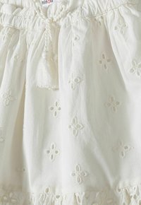 Robe en coton blanc avec des motifs floraux en broderie anglaise, taille froncée avec cordon de serrage et délicates franges au bas.