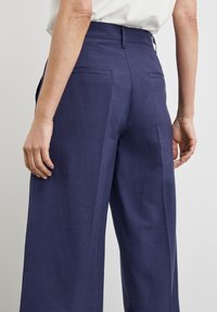 Marineblauwe linnen broek met een hoge taille en wijde benen. Voorzien van achterzakken en een soepele textuur, benadrukt door subtiele stikseldetails.