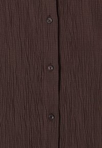Tissu marron texturé avec un motif froissé et trois boutons foncés alignés verticalement au centre.